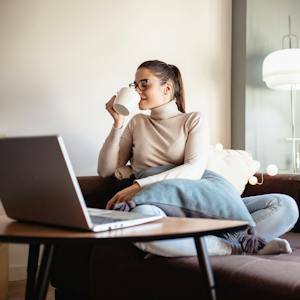 Frau arbeitet zu Hause bequem auf einem Sofa mit einem Laptop.