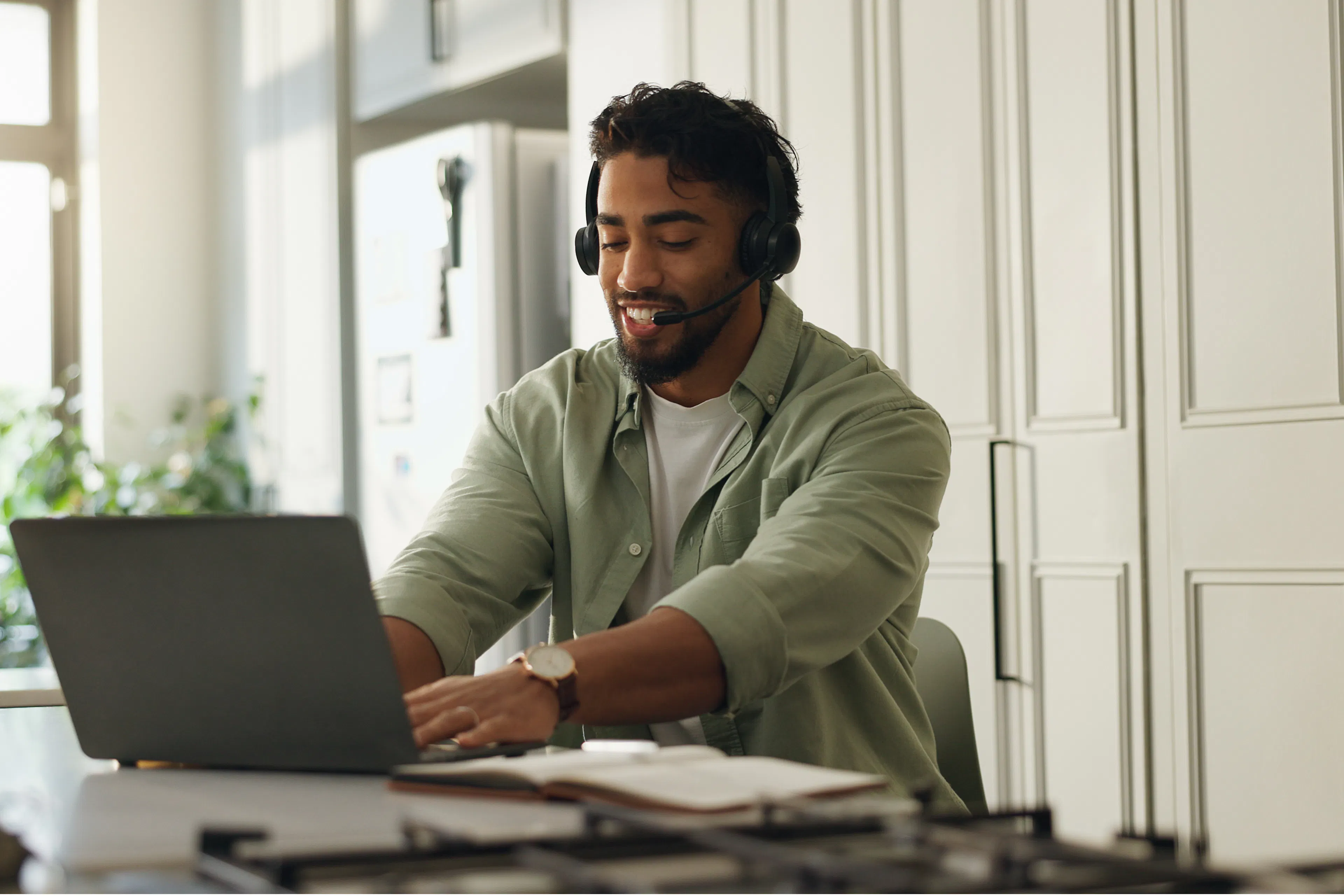 Man wearing a headset working on a laptop in a bright living space