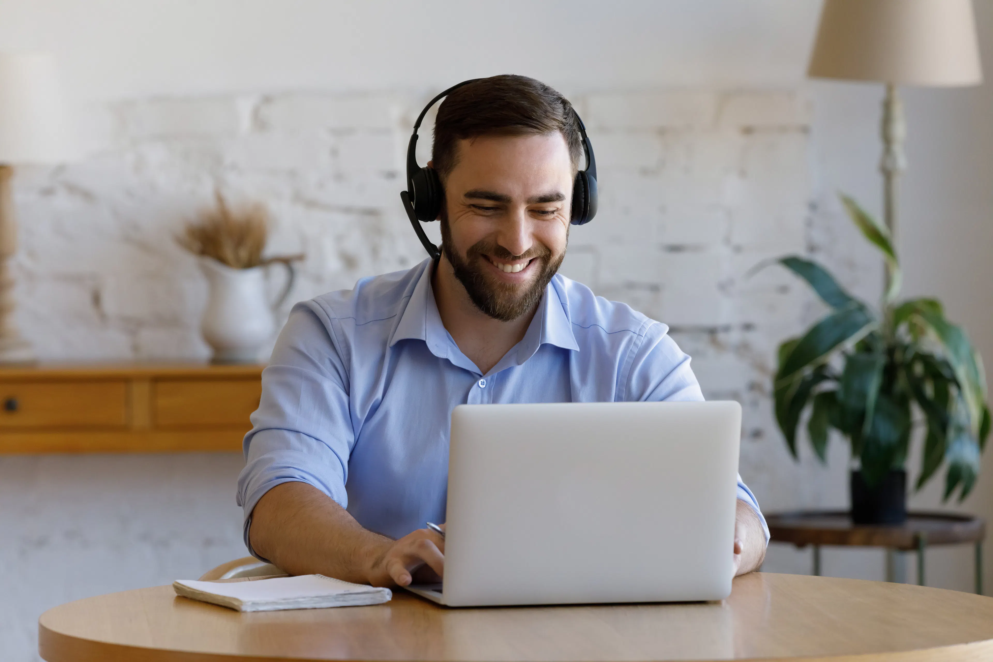 Hombre con auriculares con micrófono sonríe durante una llamada con un cliente en casa