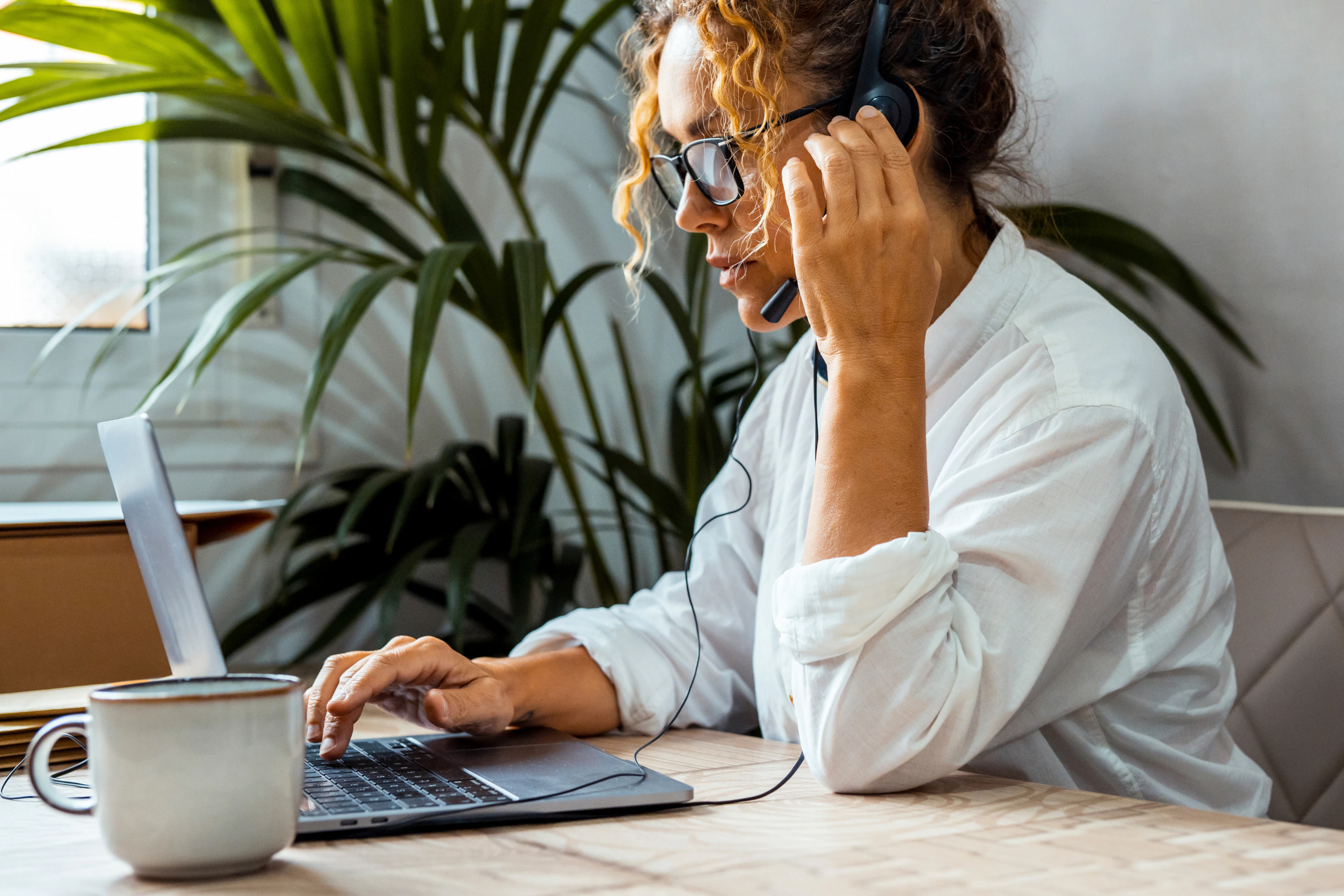Freelancerin mit Headset arbeitet im Homeoffice am Laptop