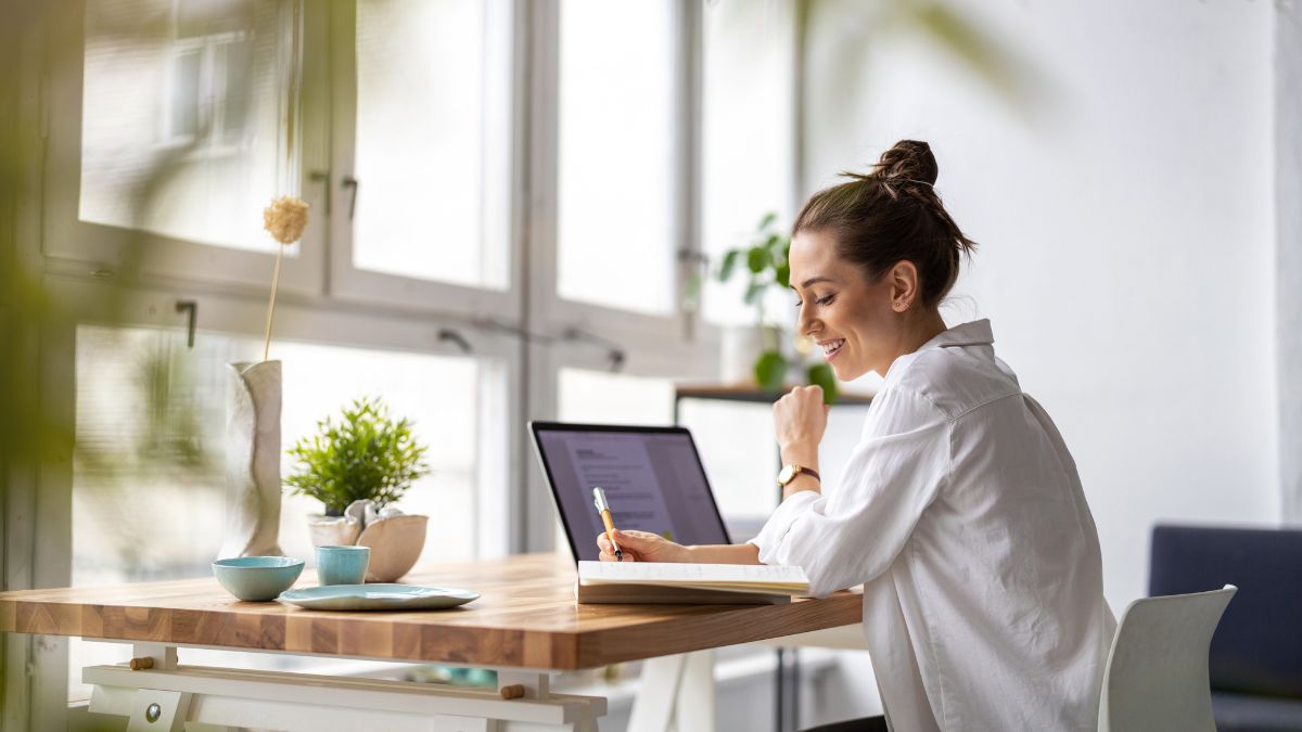 Woman working on a laptop at a desk by a large window