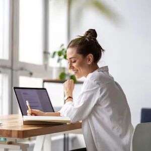 Frau arbeitet an einem Laptop an einem Schreibtisch vor einem großen Fenster