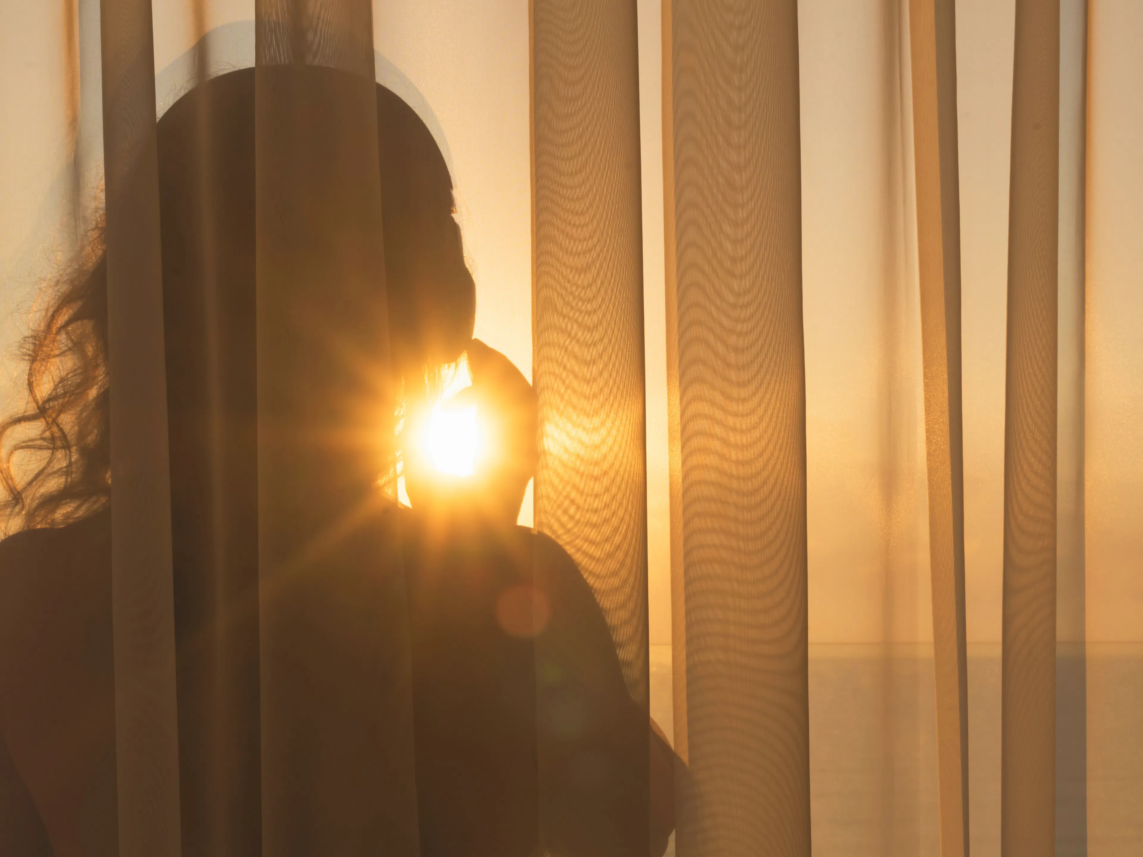 Silhouette einer Person hinter einem Vorhang im Gegenlicht der Abendsonne